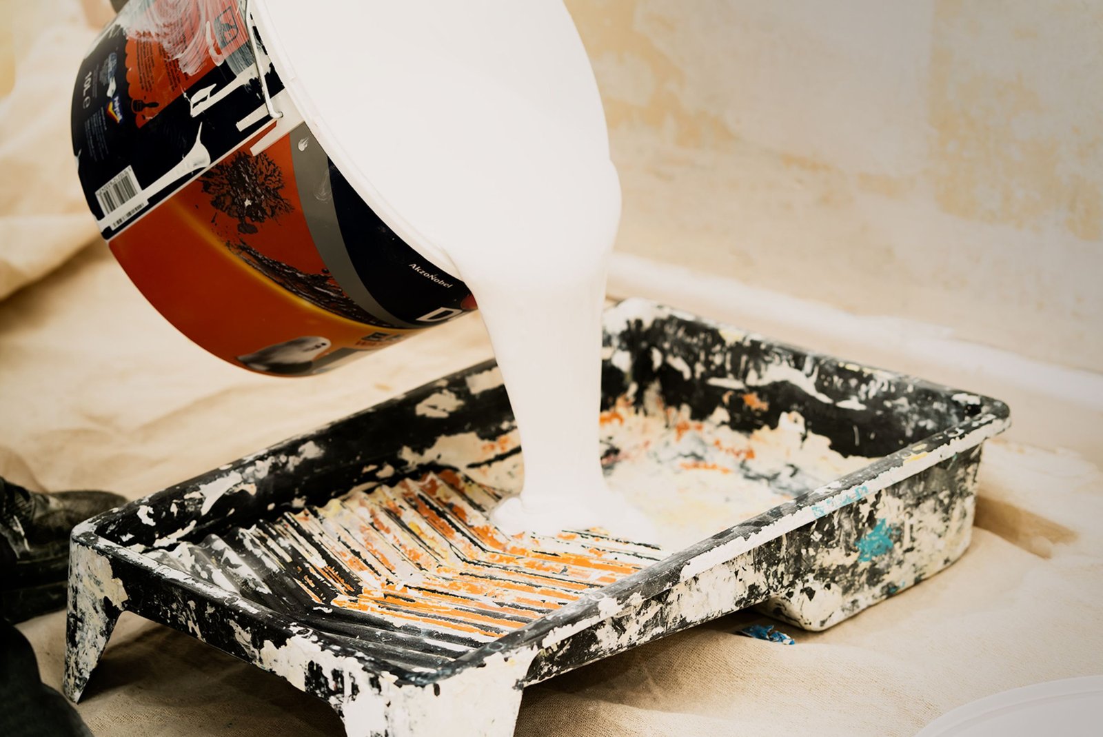 Un peintre applique une peinture airless sur un mur intérieur, pistolet en main, dans un salon en rénovation.